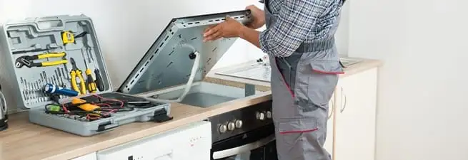 Cooktop repair technician lifting a built-in stovetop for service in Orlando, FL