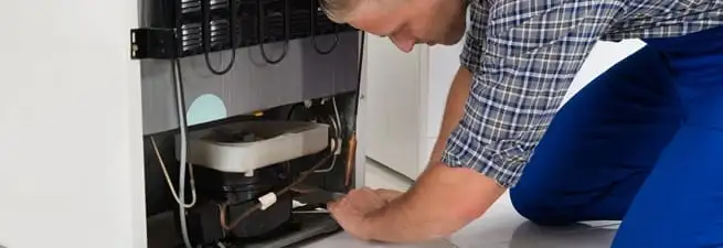 Refrigerator repair technician servicing the compressor and condenser area in Orlando, FL
